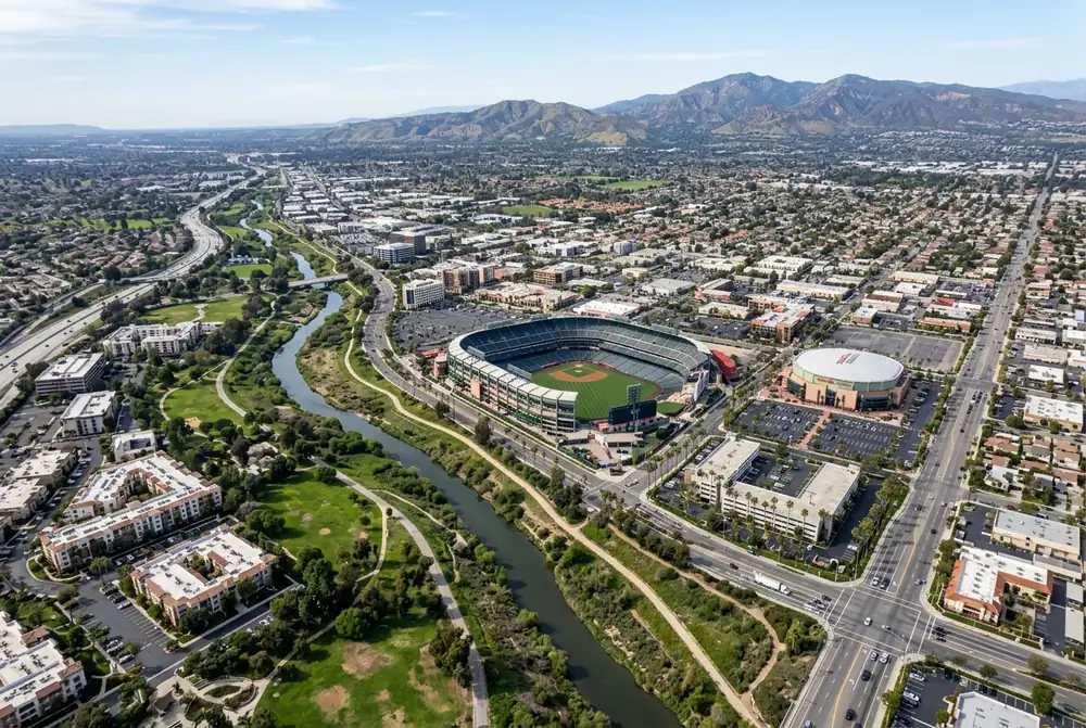 Aerial daytime view of Anaheim California showing the Platinum Triangle with Angel Stadium and Honda Center alongside the Santa Ana River and Saddleback Mountains on the horizon