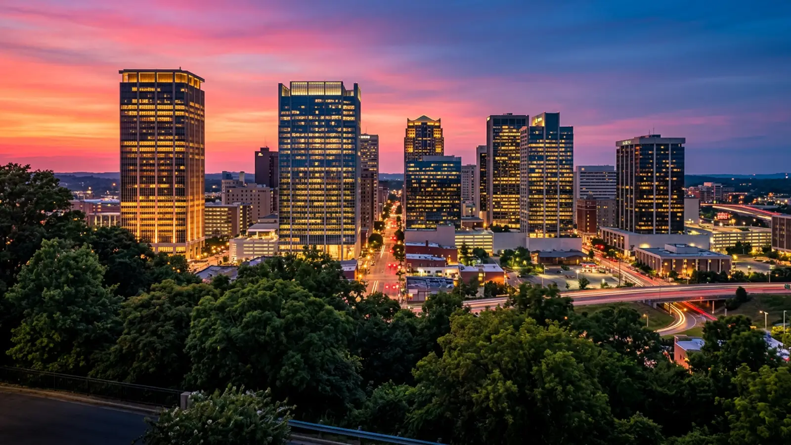 Birmingham Alabama downtown business district at twilight with modern glass office towers and lush green tree canopy in the foreground
