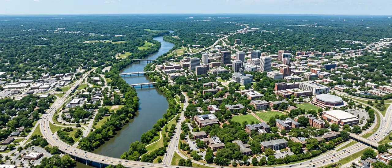High aerial daytime view of the Columbia South Carolina region along the Congaree River, with the downtown skyline, the State House dome, the University of South Carolina campus, the river confluence, and the surrounding green suburbs of Lexington and Richland counties under a clear summer sky