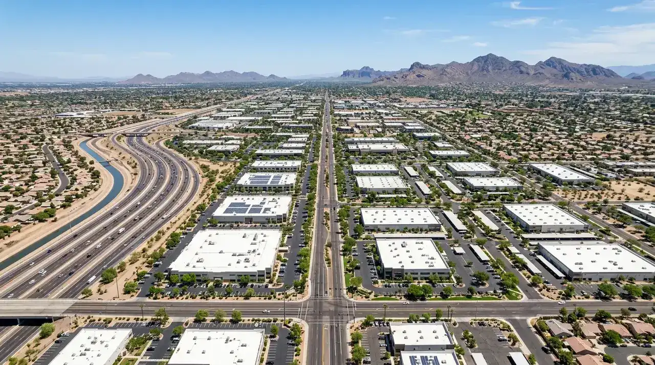 High aerial daytime view of the East Valley of metropolitan Phoenix Arizona, showing a grid of wide streets, green landscaped corporate and light industrial campuses, a multi-lane freeway, an irrigation canal, and distant desert mountains