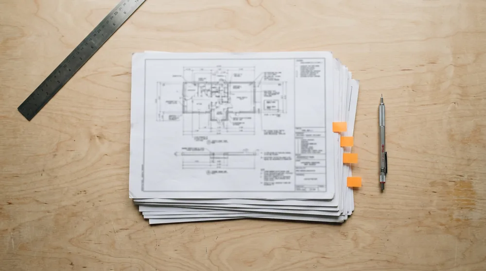 Stack of printed engineering change drawings with orange index tabs on a San Jose workbench