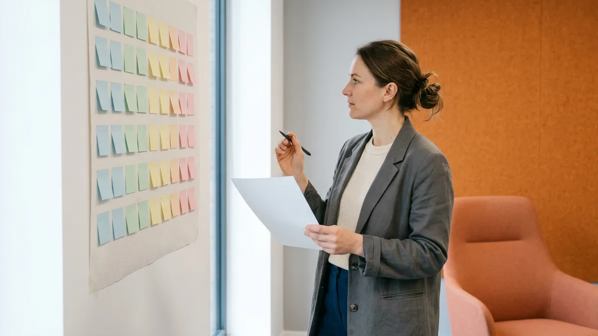 Recruiting coordinator rebuilding an interview panel schedule against a paper wall calendar, printed candidate itinerary in hand