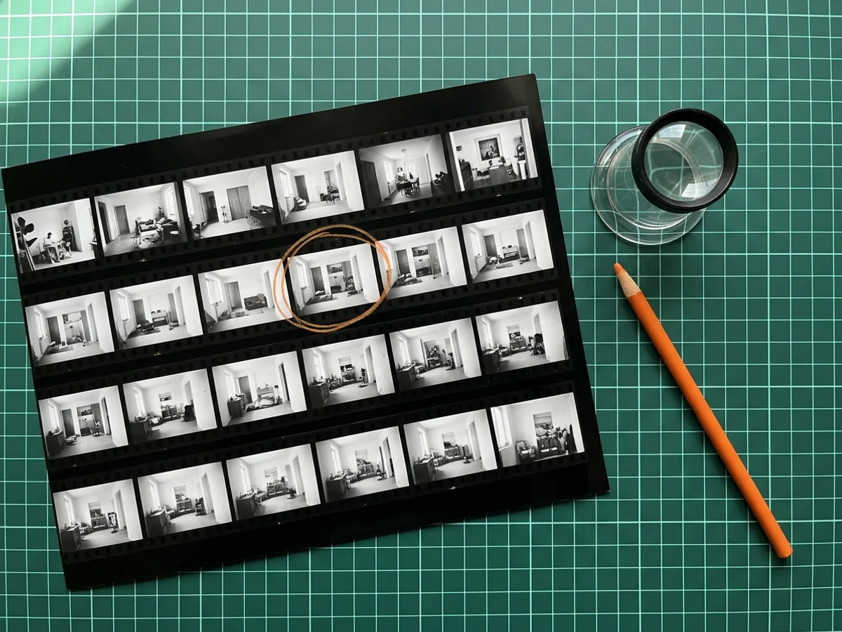 Black and white contact sheet with one frame circled in orange grease pencil, a glass loupe and an orange china marker on a green cutting mat