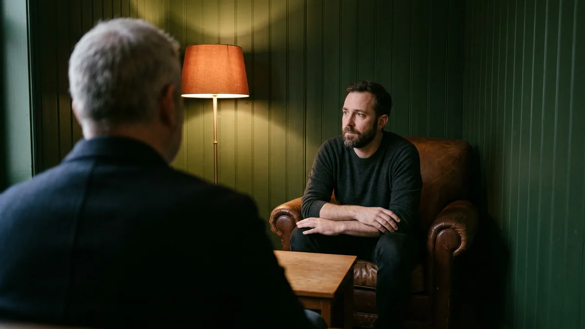 Bearded candidate in a leather armchair thinking through a blockchain developer interview question, seen over the interviewer's shoulder