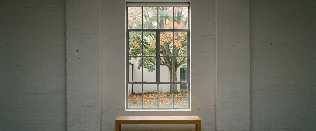 Empty whitewashed studio with a tall steel window looking onto a half-turned autumn tree, for a post on hard-to-fill positions that stay open for months