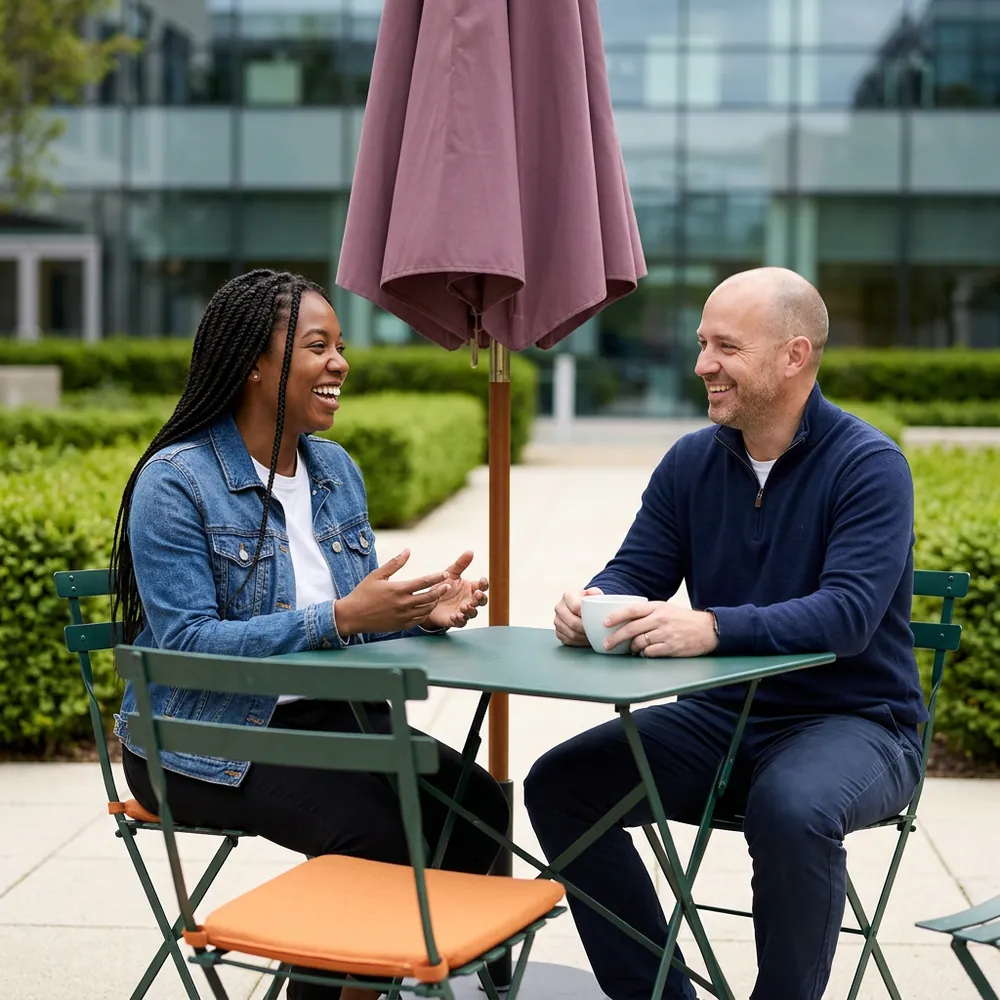 Data engineer and claims analyst laughing at a bistro table under a plum umbrella in an office courtyard