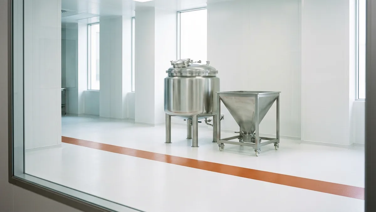 Empty GMP pharmaceutical manufacturing suite with a stainless steel vessel and hopper seen through an inspection window