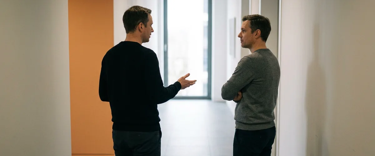 Two colleagues standing in an office corridor discussing how to hire an Informatica developer