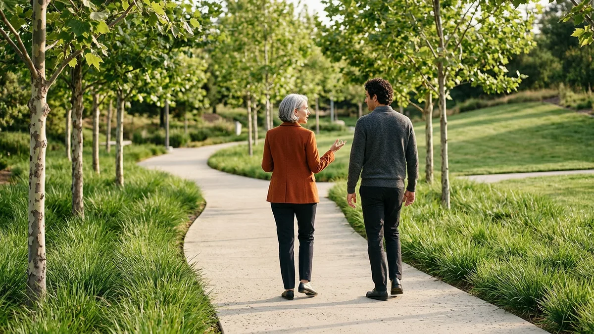 Vendor delivery lead in an orange blazer talking with a client engineering leader while walking a tree-lined campus path