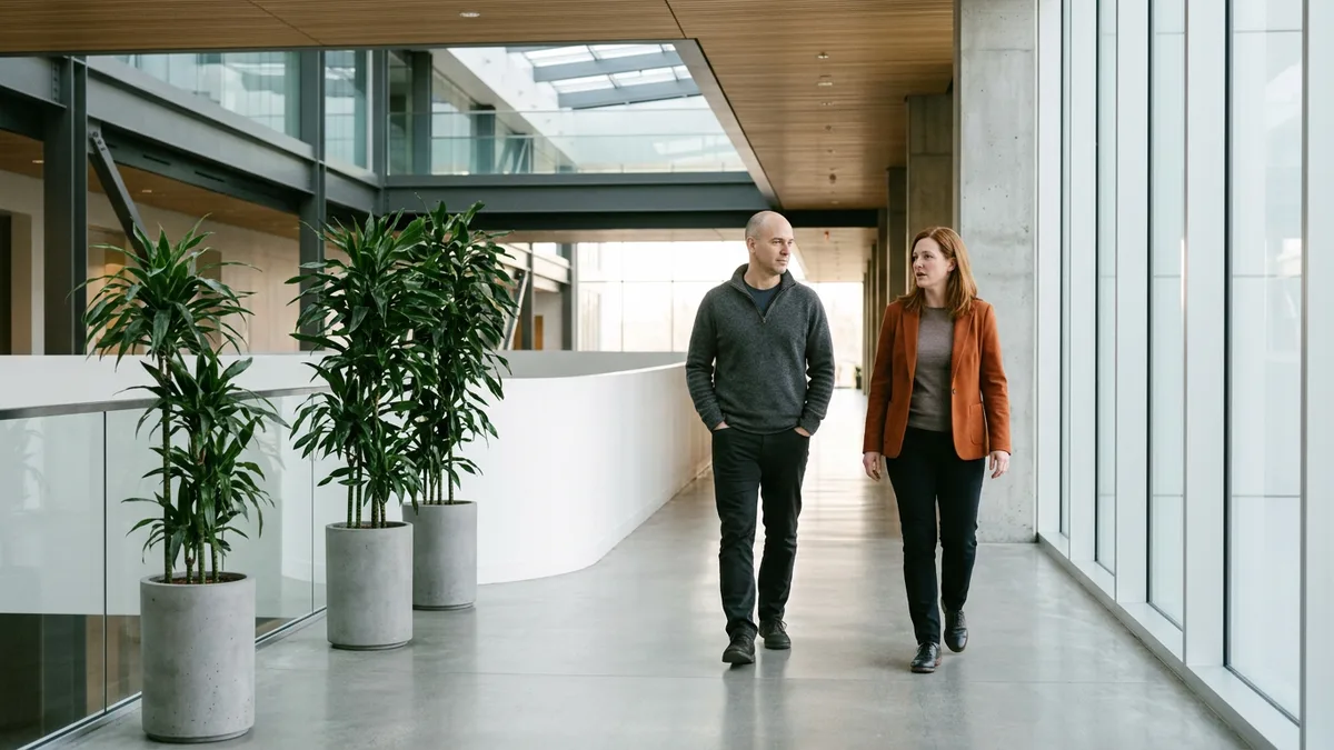Non-technical business owner walking an office atrium with a senior software engineer who reviews the team code