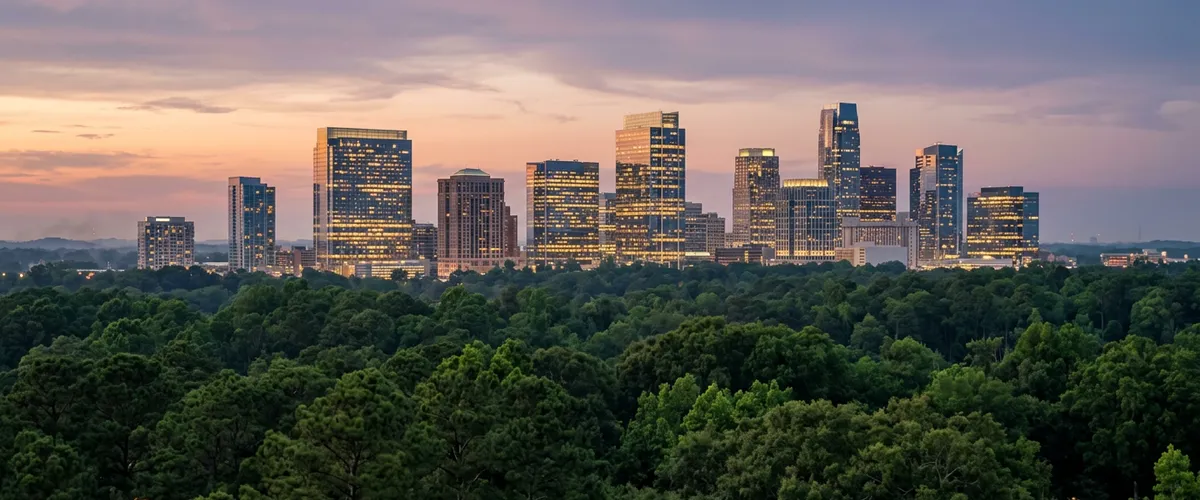 Charlotte skyline at dusk seen across a canopy of trees south of Uptown