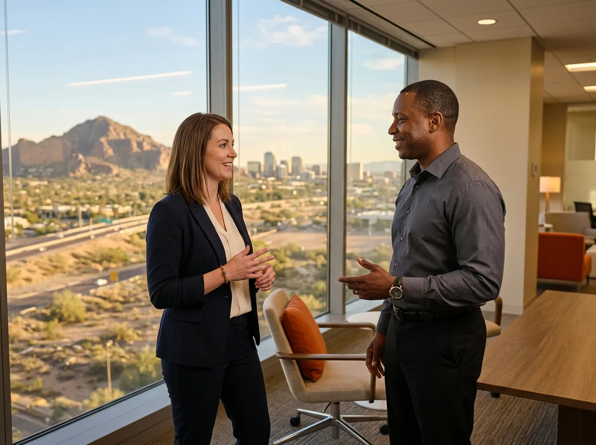 A KORE1 recruiter and a Phoenix hiring manager talking beside a floor-to-ceiling window with Camelback Mountain and the desert skyline behind them
