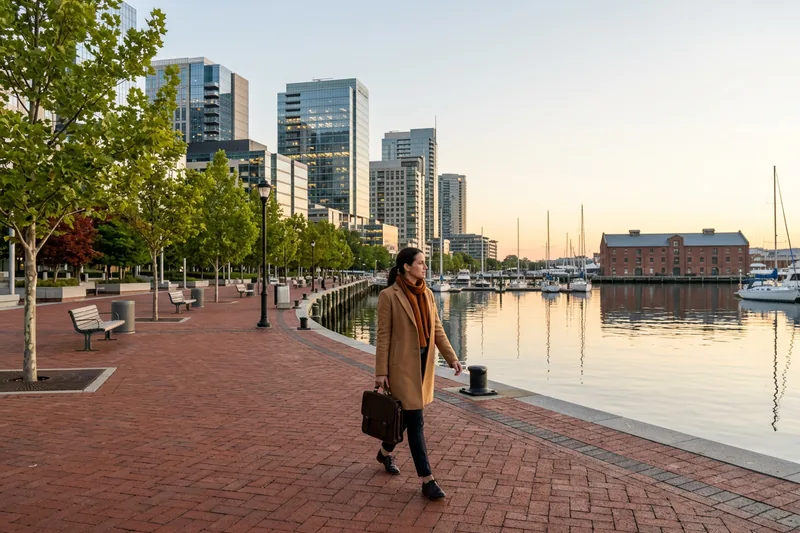 Finance professional walking the Harbor Point waterfront promenade toward glass office towers in Baltimore