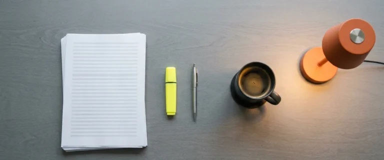 Overhead view of a desk with a printed software vendor spend report, highlighter, pen, coffee mug and orange desk lamp