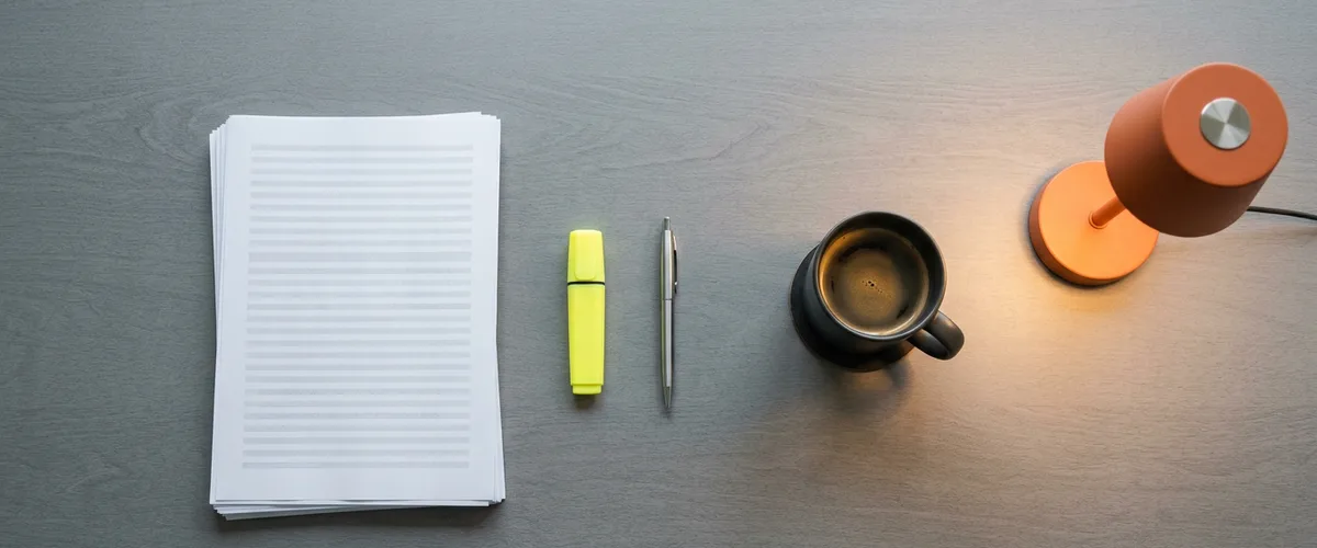Overhead view of a desk with a printed software vendor spend report, highlighter, pen, coffee mug and orange desk lamp