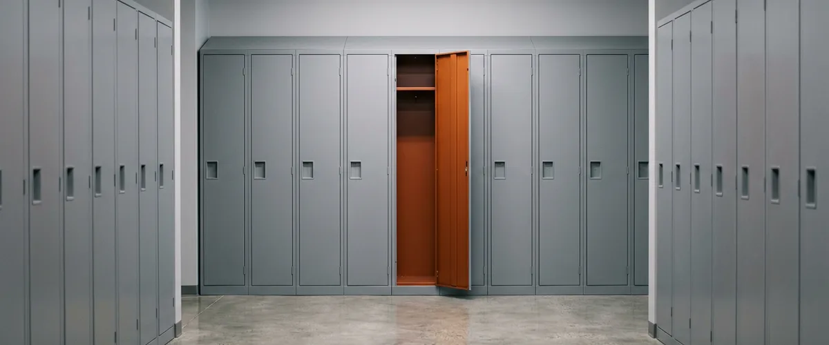 Row of identical gray steel lockers in an office corridor with a single locker door standing open to a burnt orange interior