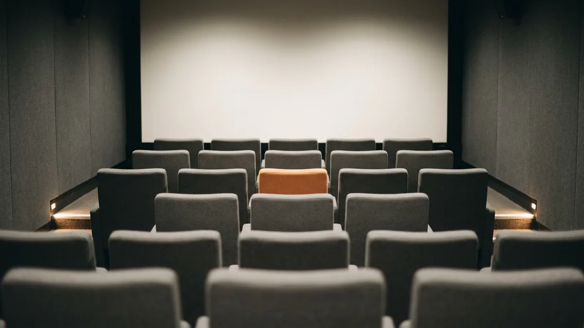 Empty private screening room with rows of grey seats and a single orange seat, representing creative director pay in film and video