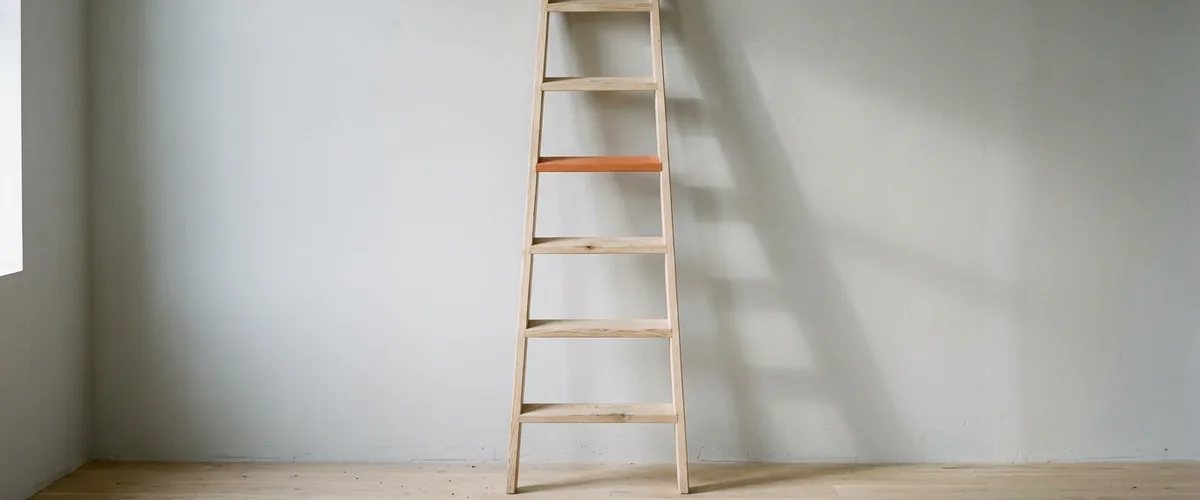 Plain wooden step ladder leaning against a pale grey wall with one rung painted orange, illustrating creative director pay by title level