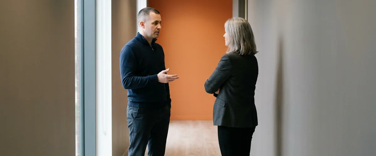 IT support lead explaining monthly help desk coverage costs to an operations director in an office corridor