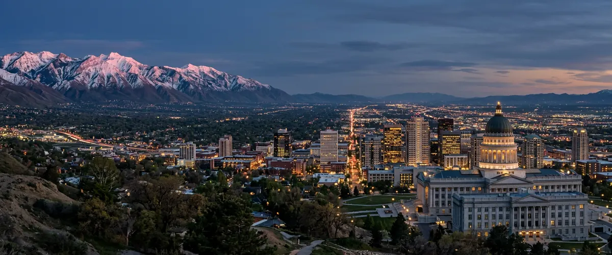Downtown Salt Lake City and the Utah State Capitol at dusk with the snow capped Wasatch Range glowing in alpenglow and the valley lights stretching south