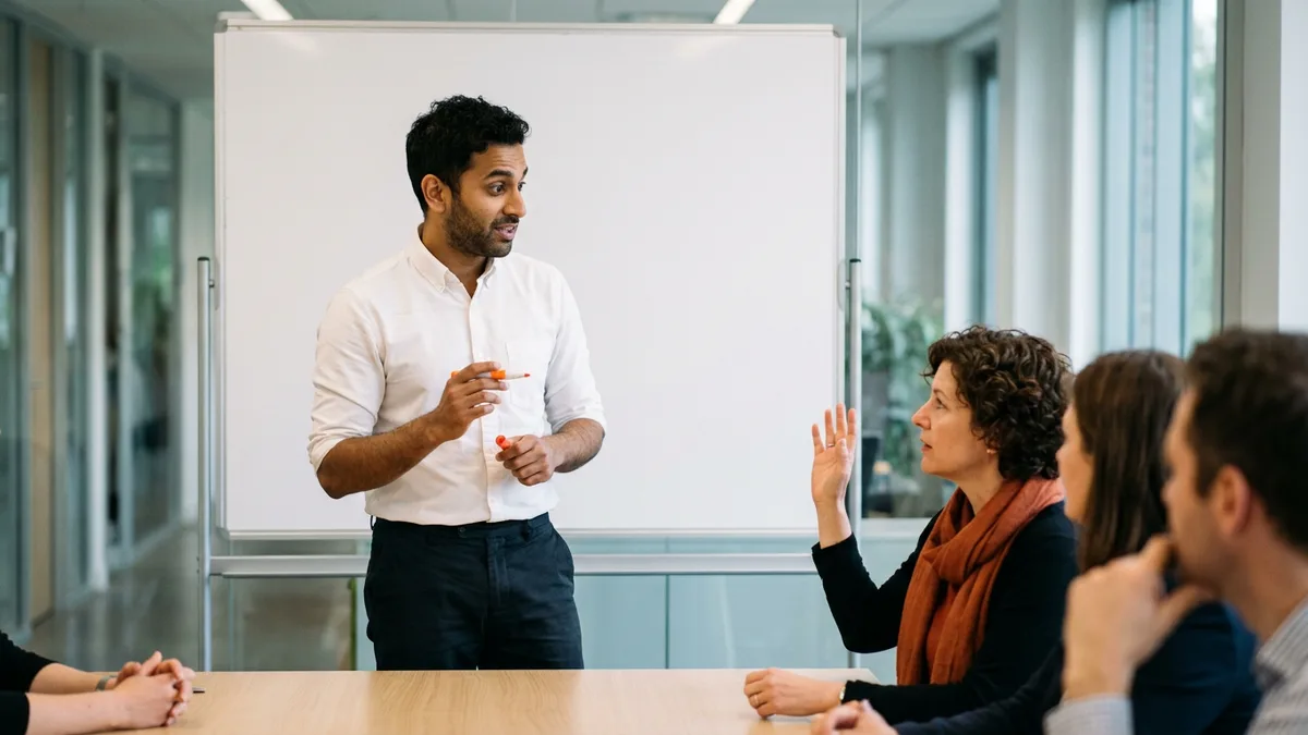 Interview panel member in an orange scarf raising her hand to interrupt a sales engineer candidate presenting at a whiteboard