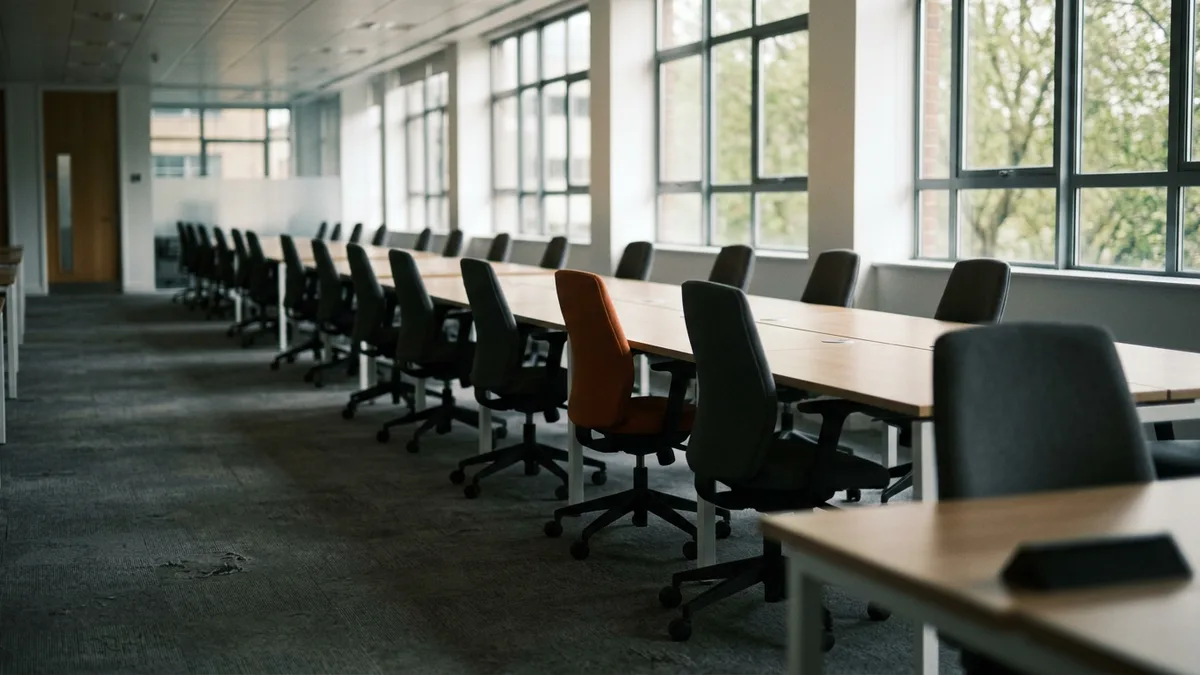 Row of empty desks and chairs in a quiet open-plan office, the open seats a funded Salesforce project still needs to fill