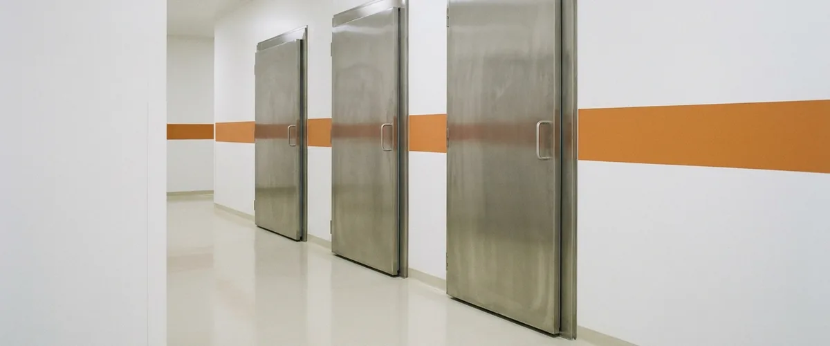 Corridor in a pharmaceutical facility with three stainless steel walk-in stability chamber doors beside an orange wall stripe